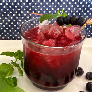 Blueberry mojito drink in a glass garnished with blueberries and mint leaves with blue dotted background.
