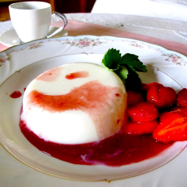 Strawberry panna cotta on a white plate with fresh strawberries and strawberry sauce.