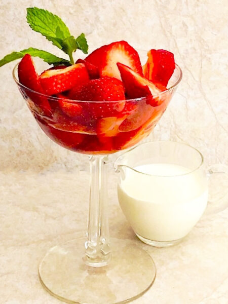 Parfait glass with fresh sliced strawberries and a sprig of mint with a small pitcher of cream on the side.