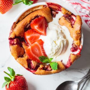 Strawberry cobbler with ice cream in a round bowl.