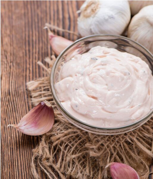 Aioli sauce with mayonnaise and crushed garlic in a glass dish on a woven mat.