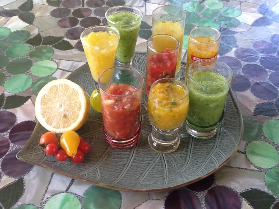 A range of different flavored gazpacho shots on a round grey serving board.
