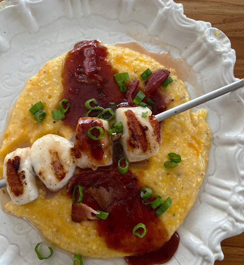 Skewer of grilled scallops on a bed of polenta drizzled with tomato jam