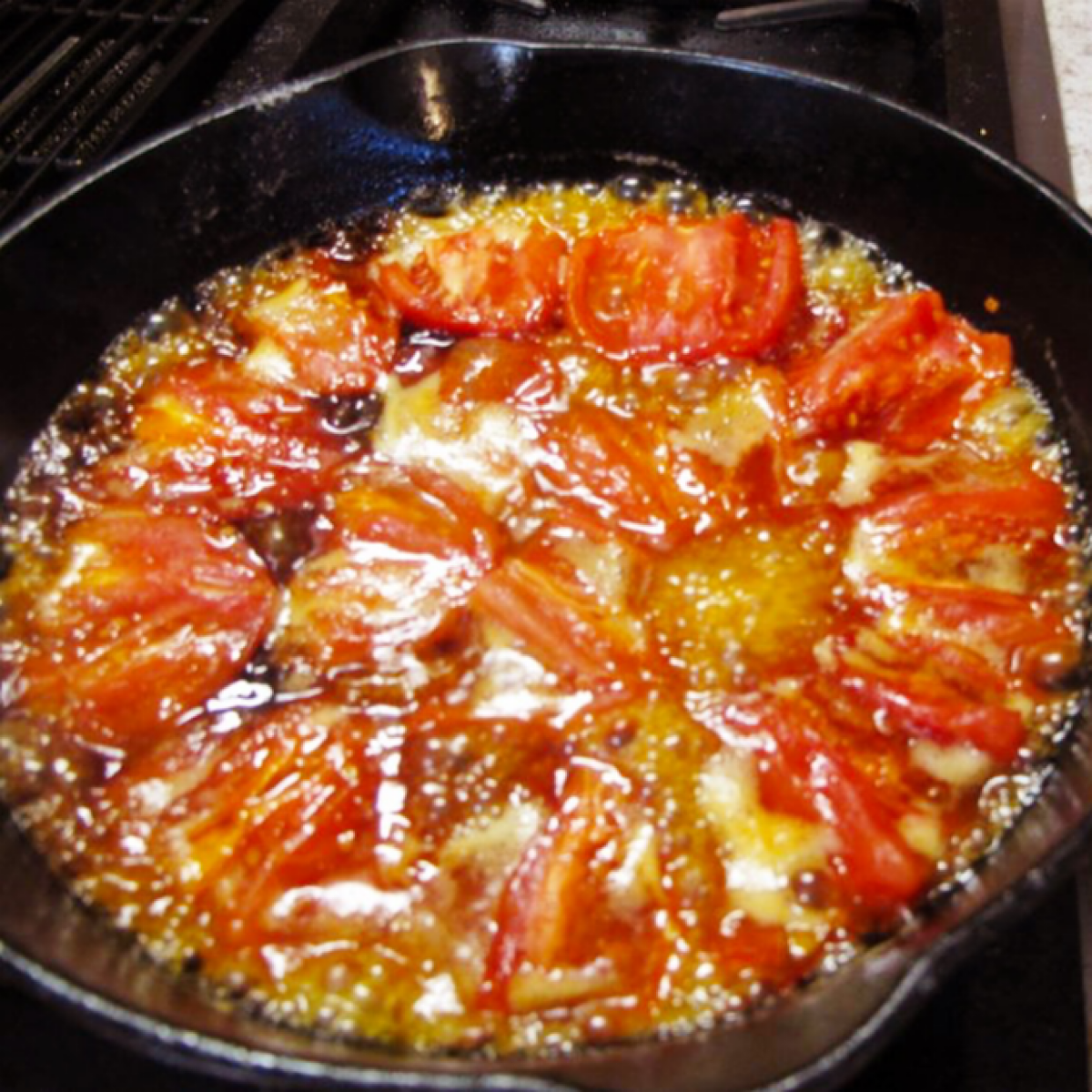 Sliced roma tomatoes cooking in butter and sugar in a skillet.