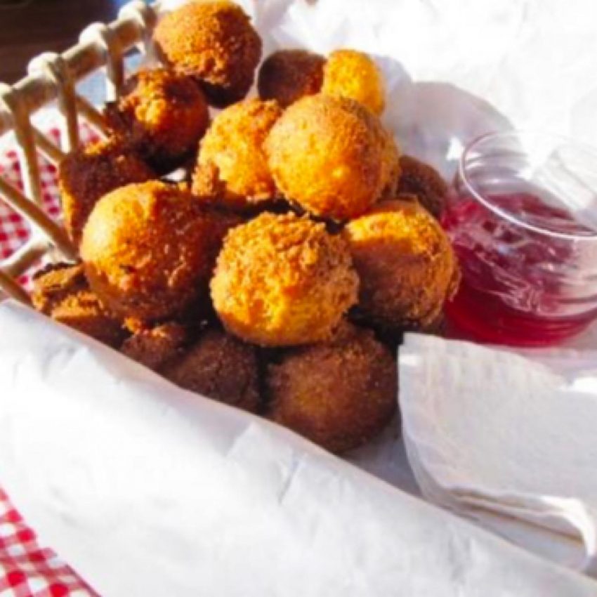 Hush puppies in a basket with red pepper jelly as a dipping sauce