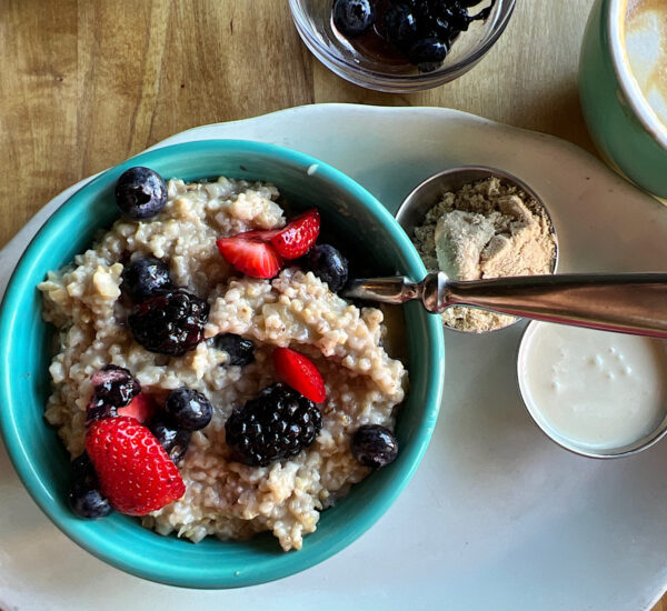 Oatmeal in a blue bowl topped with strawberries and blackberries with sugar and cream on the side.