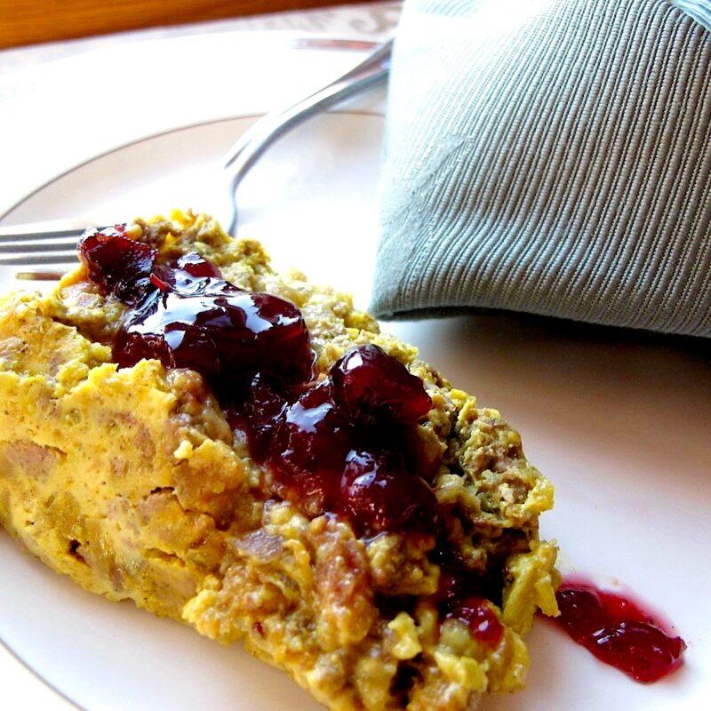 Slice of savory meat pie called bobotie topped with cranberry chutney.