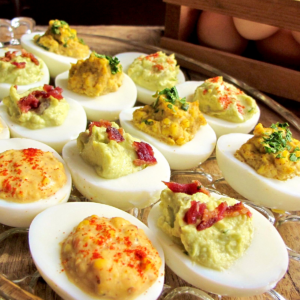 Plate of deviled eggs in rows of 3 different fillings: harissa, avocado and bacon and curry.