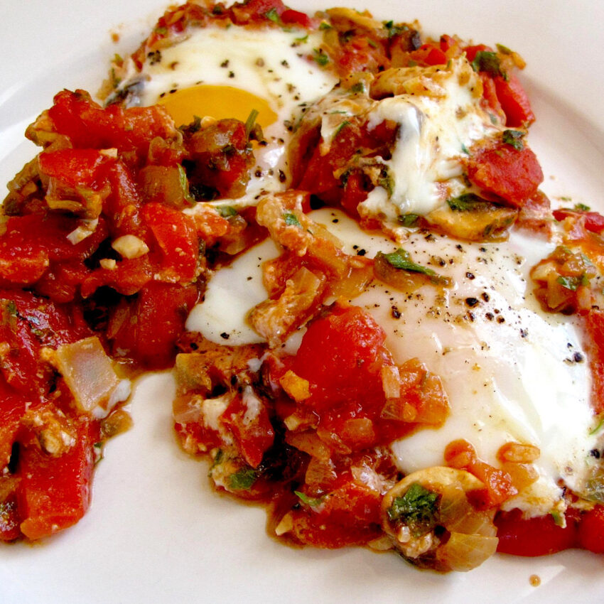 Mediterranean baked eggs with tomatoes and spices on a white plate.