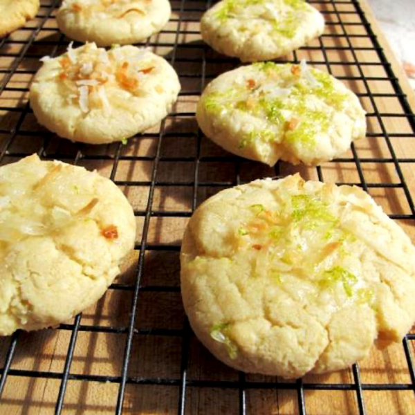 Coconut cookies with citrus icing and lime zest topping on a wire baking rack.