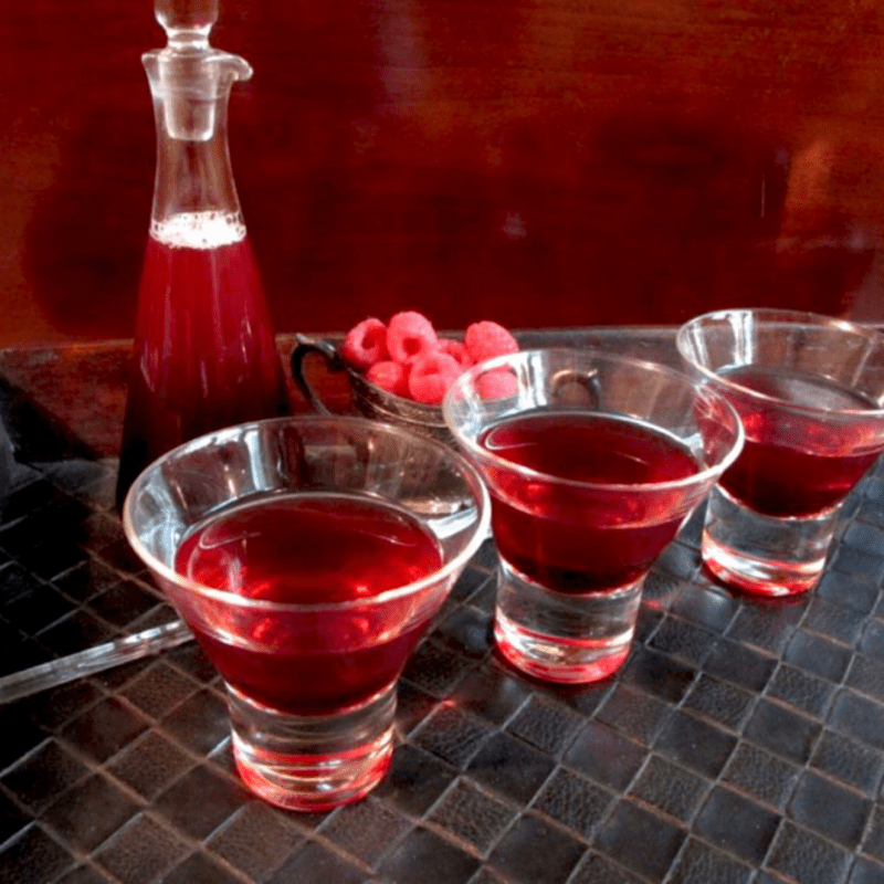 3 raspberry martinis with raspberry syrup in the back ground on a dark tray.
