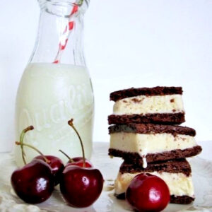 Homemade ice cream sandwiches with cherries in front and a jug of milk to the side.