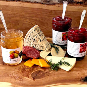 3 jams with spoons in them surrounding a range of cheeses on a cheese board.