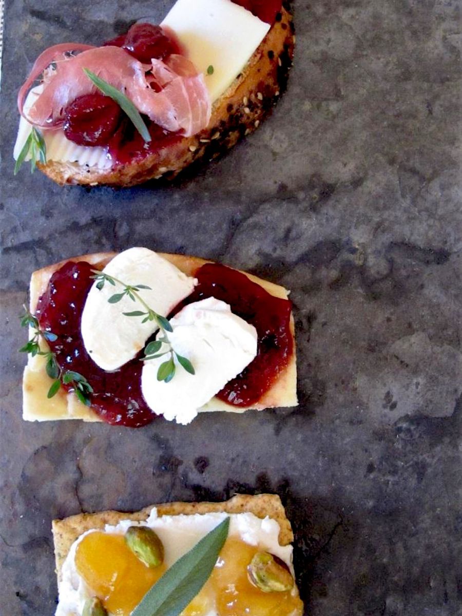 Cheese platter showing combinations of crackers, cheese, jams and herbs as appetizers.