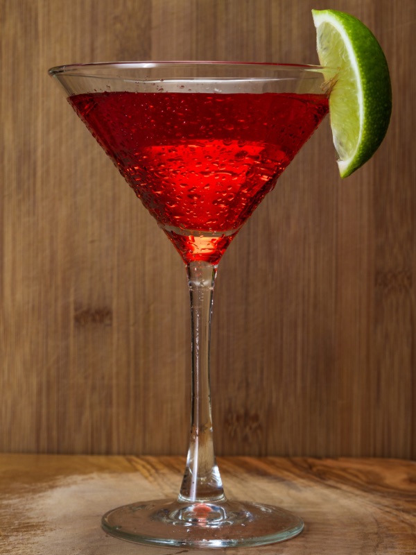 Cranberry martini with cranberry drink syrup, garnished with lime wedge.