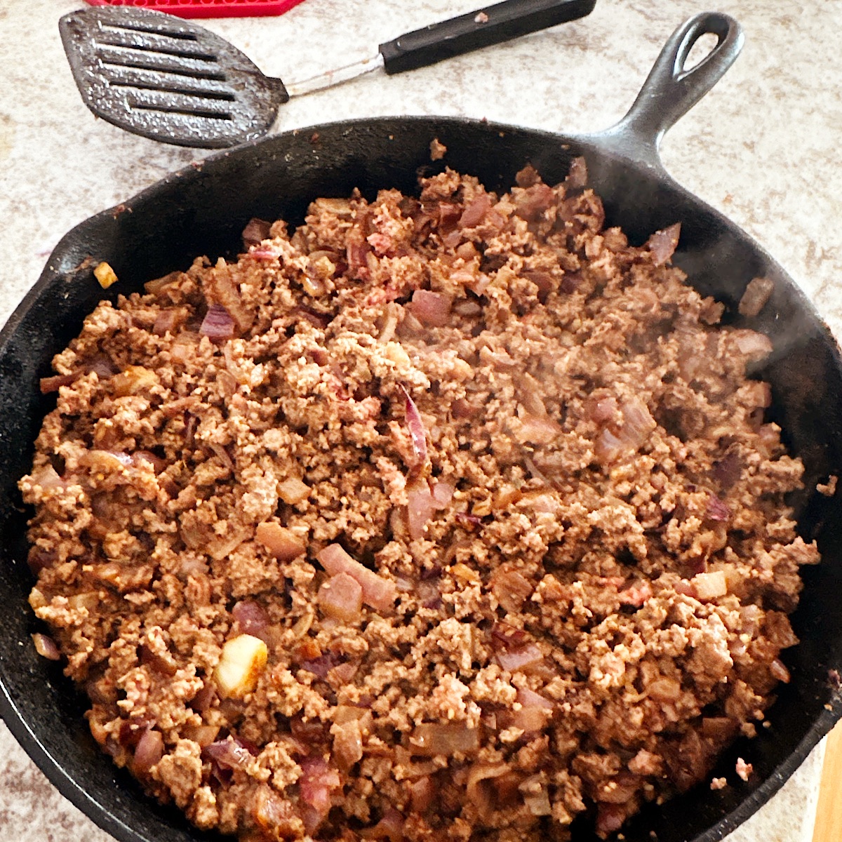 Ground beef, onions and spices cooking in black cast iron skillet.