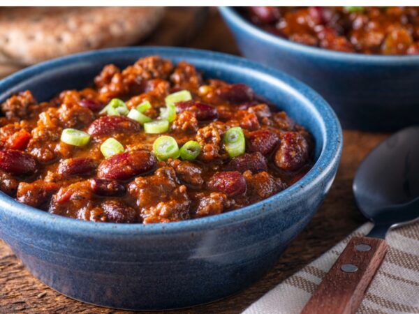 Beef and bean chili garnished with scallions in a blue bowl.
