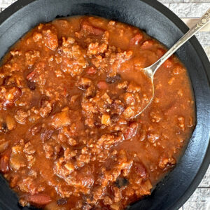 Spicy beef and bean chili in a black bowl with a silver spoon.