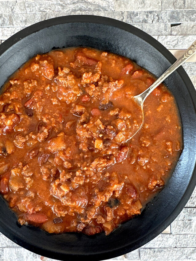 Spicy beef and bean chili in a black bowl with a silver spoon.