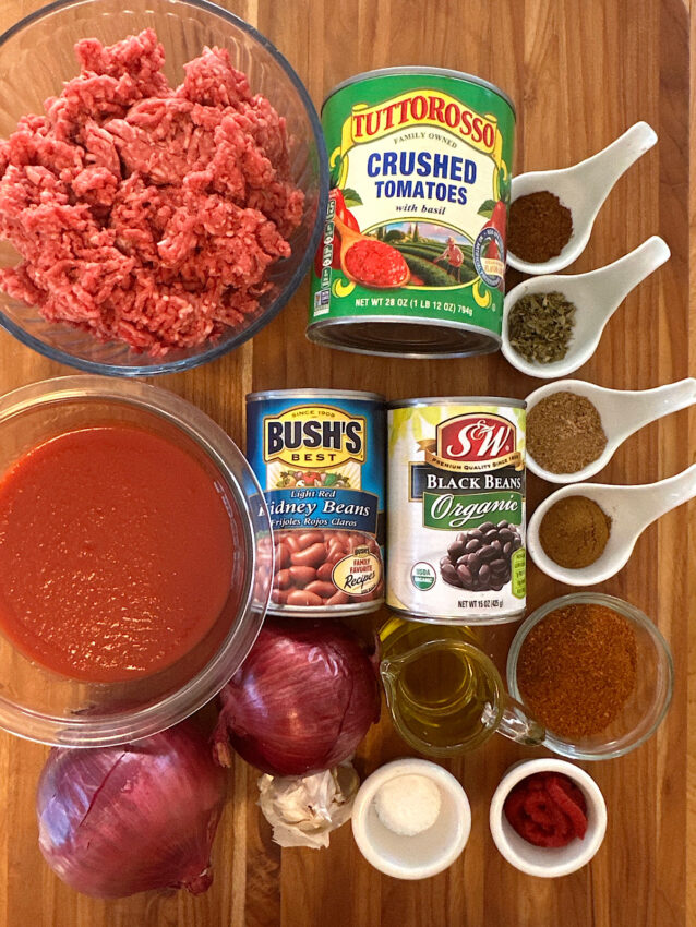 Ingredients for beef and bean chile laid out on a wood cutting board.
