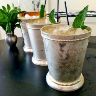 3 silver julep glasses with cold mint julep cocktails and mint in background.