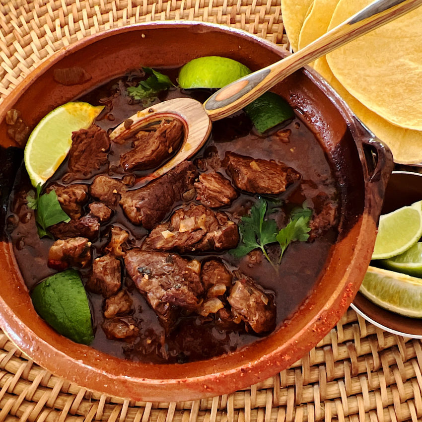 Low carb chile Colorado in a bowl surrounded by corn tortillas and lime wedges.