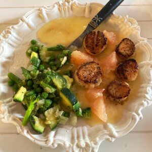 Dinner plate of seared scallops in grapefruit-butter sauce with side of green vegetables