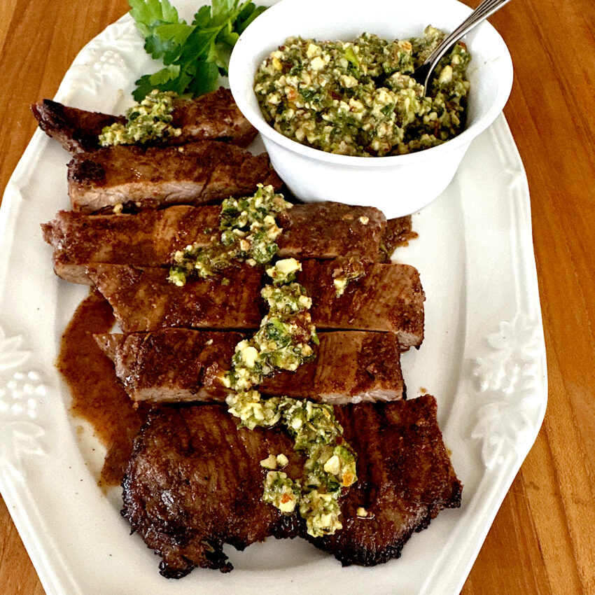 Pan seared skirt steaks topped with chimichurri sauce with a side of chimichurri in a small bowl.