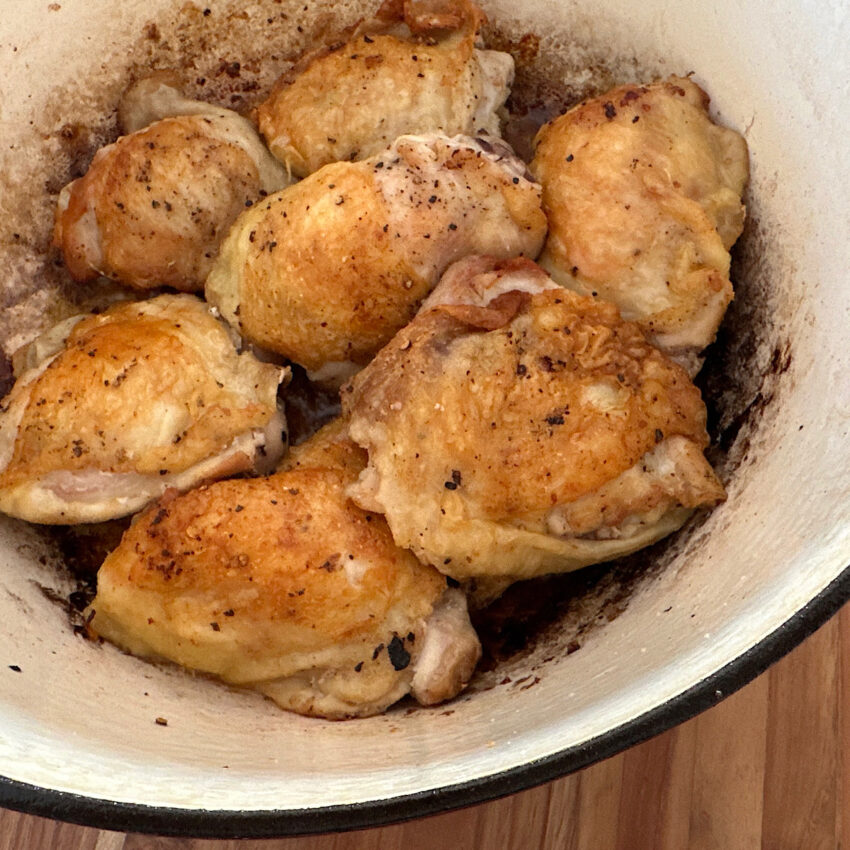 Chicken thighs browned in oil in a dutch oven.