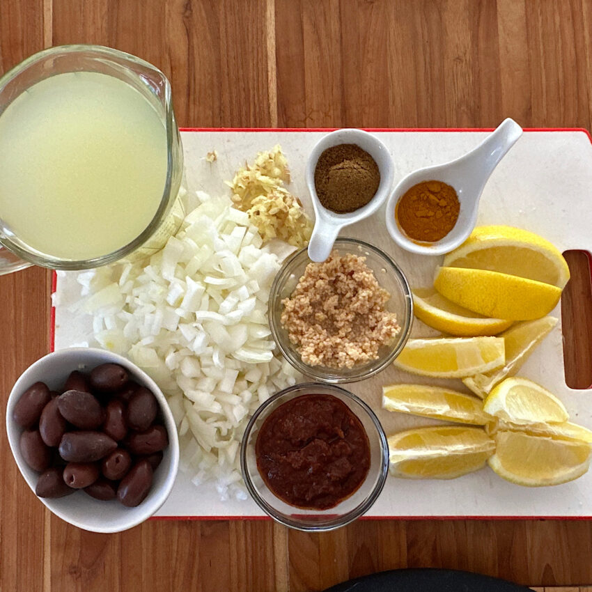 Ingredients for adding to chicken to make Moroccan chicken stew; black olives, onion,stock, spices, lemons, garlic and harissa.