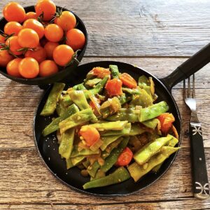 Romano beans with roasted cherry tomatoes in skillet with bowl of sun gold tomatoes on the side.