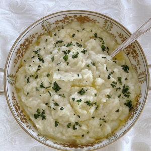 Bowl of low carb mashed cauliflower garnished with parsley.