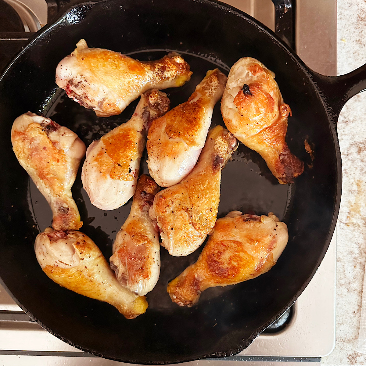 Chicken legs being browned in a cast iron skillet