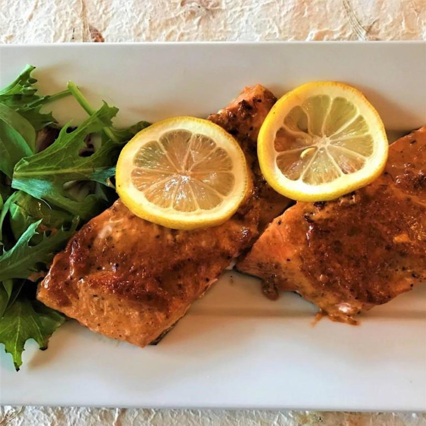 Two salmon filets glazed with a harissa sauce and topped with sliced lemons.