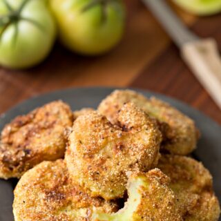 Fried green tomatoes on plate with green tomatoes in background.
