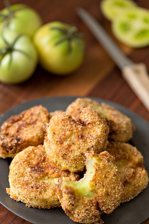 Fried green tomatoes on plate with green tomatoes in background.