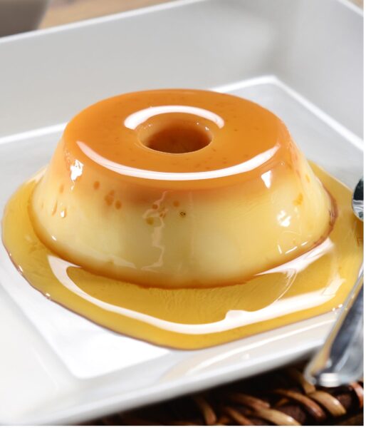 Caramel flan on a white square plate with caramel underneath the flan.