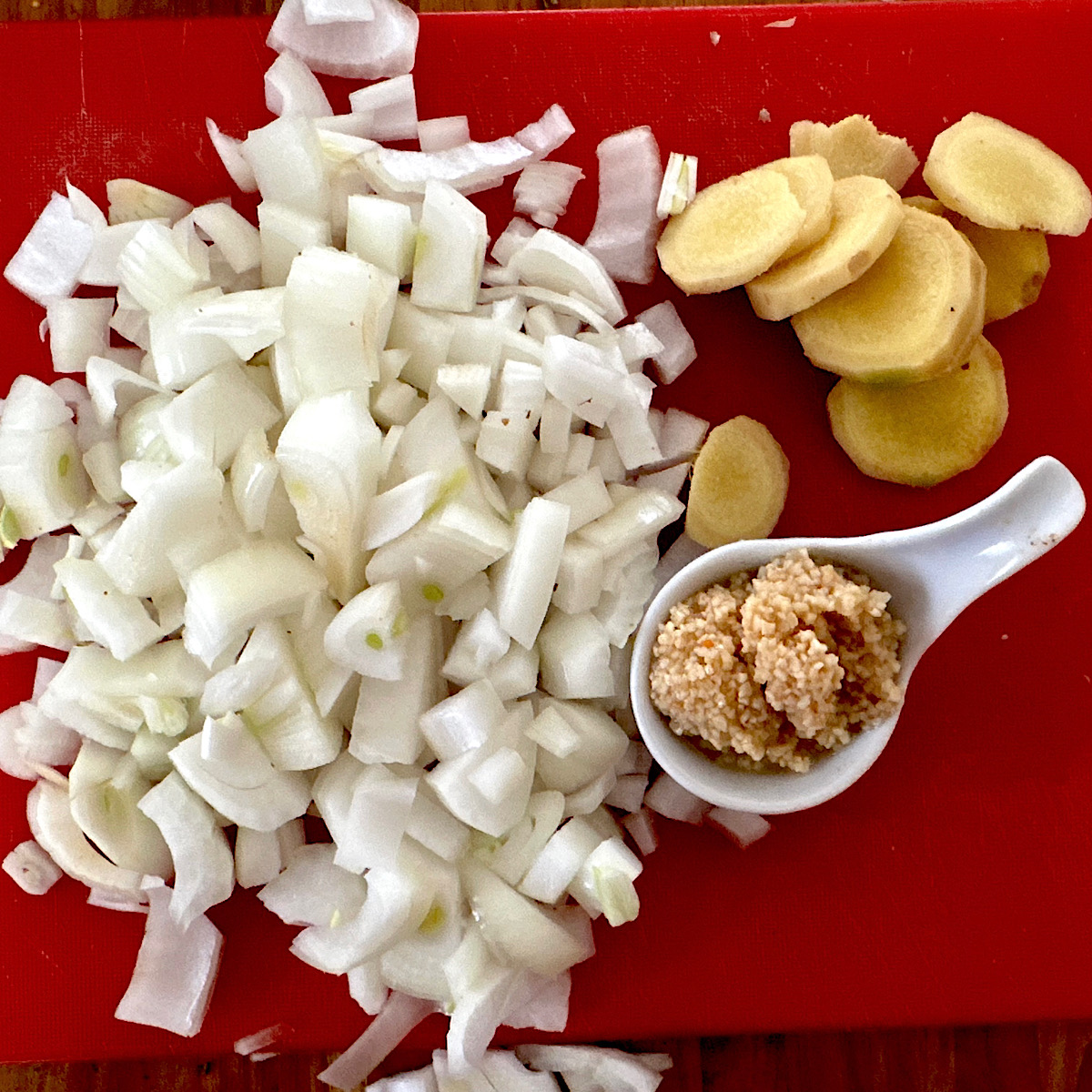 Chopped onion, slices of root ginger and a white spoon with minced garlic.