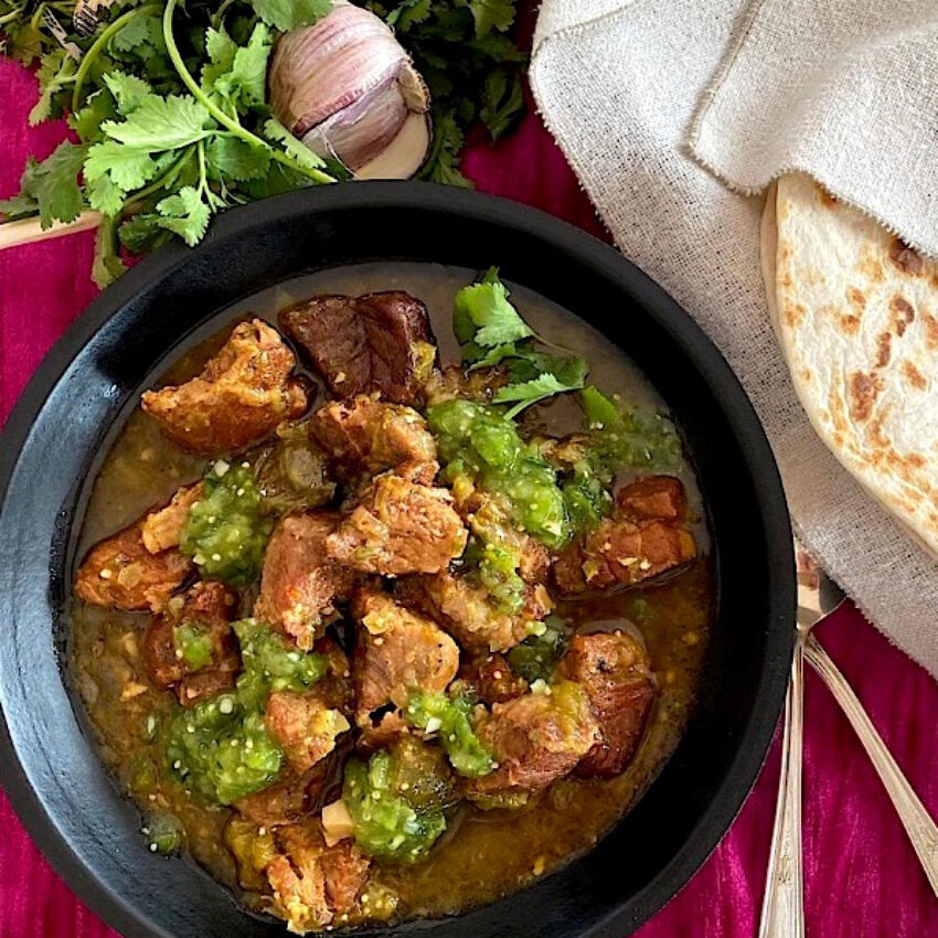 Black bowl of chile verde stew with tortillas on the side.