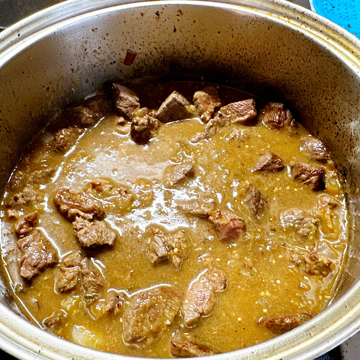 Pork chile verde cooking in a large stainless steel pot on the stove.