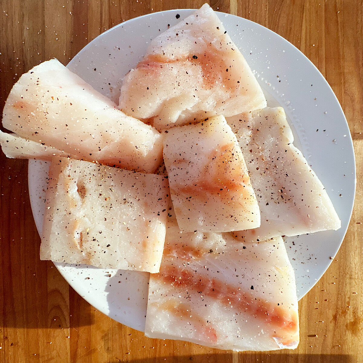 Six cod filets on a white plate on a cutting board