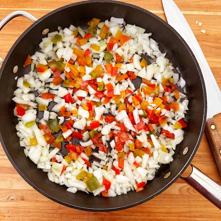 Chopped onions and bell peppers ready to cook in a large skillet.