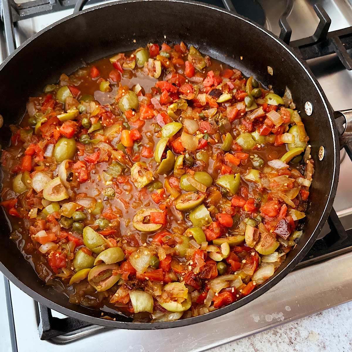 Skillet with tomatoes, olives, capers and onions simmering for fish veracruz.