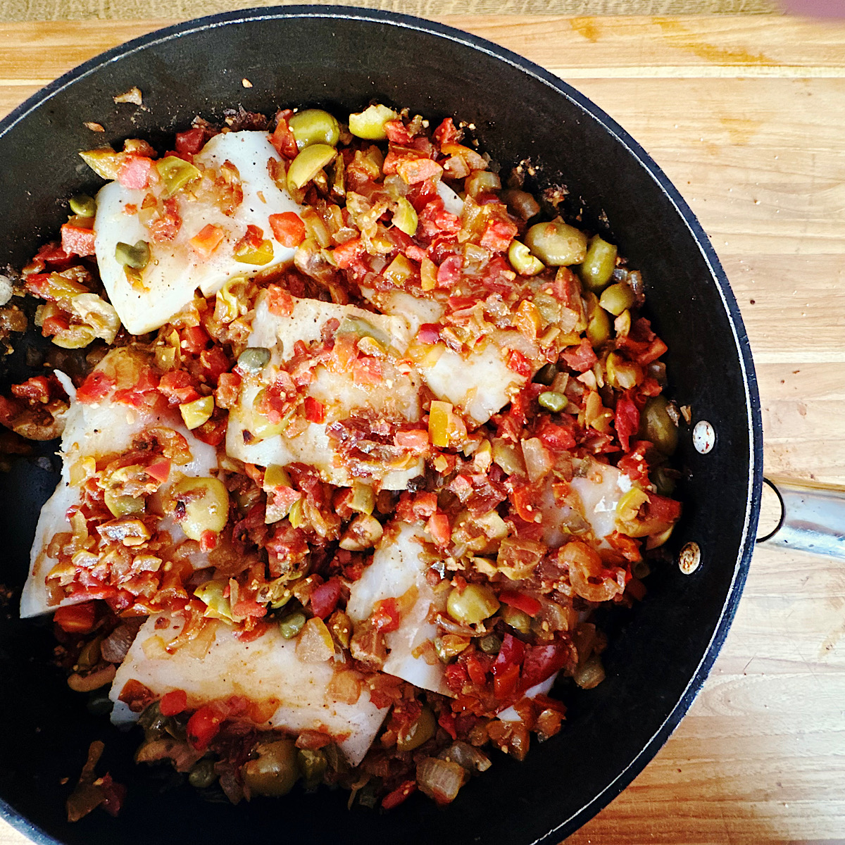 Cod filets nestled into veracruz sauce in a skillet.