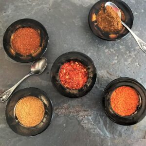 Five different powdered chile spices in black small bowls.