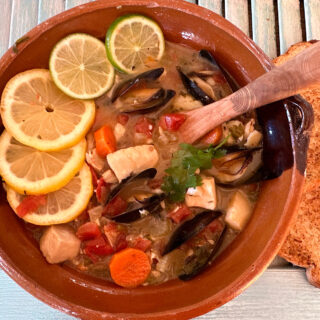 Clay bowl of Mexican Seafood Stew with carrots, tomatoes, mussels and white fish.