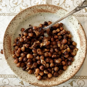 Bowl of roasted chickpeas with a spoon on a beige placemat.