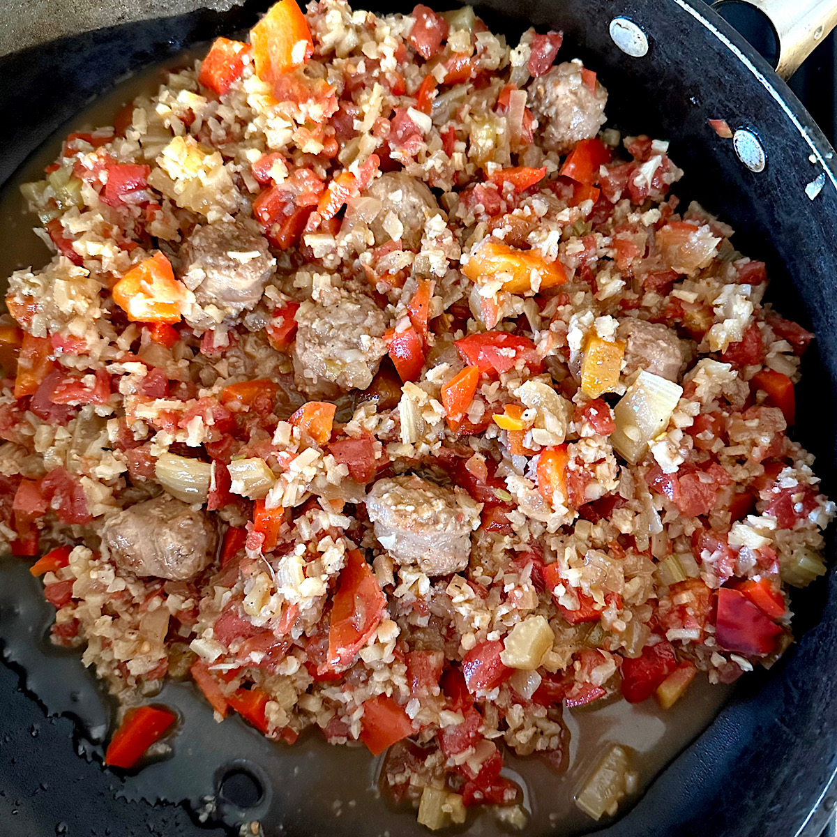 Sausage and sofrito (peppers, onion and celery) cooking in red dutch oven.