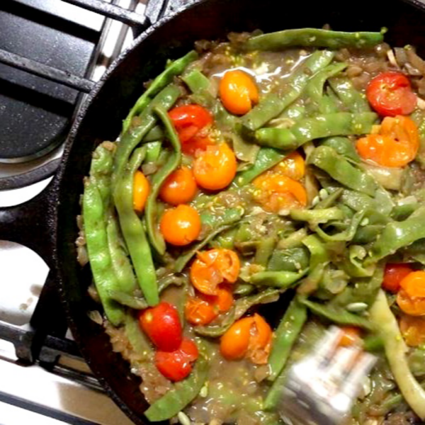 Italian flat beans cooking in a skillet with smashed cherry tomatoes