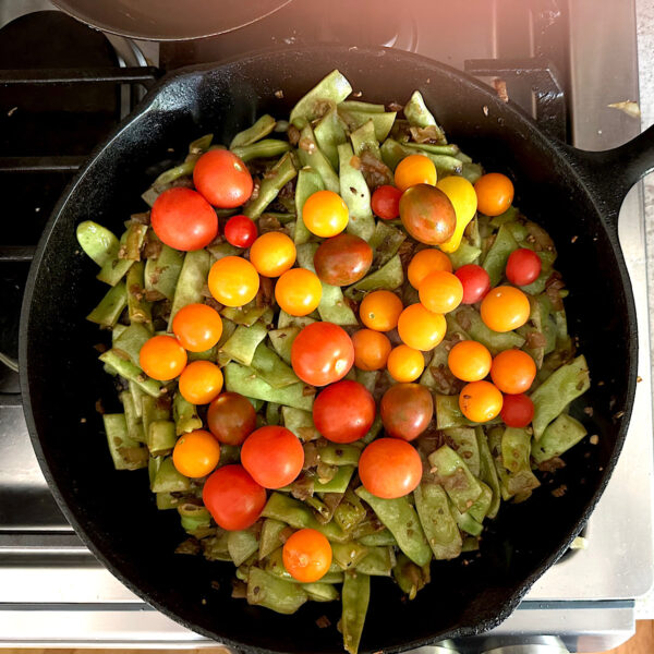 Cherry tomatoes and flat beans simmering in skillet.